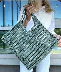 a woman holding a green crocheted bag in front of a window with her hand on the handle