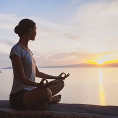 a woman sitting on the edge of a cliff doing yoga