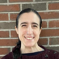 a woman smiling in front of a brick wall with her hair pulled back and wearing a maroon sweater