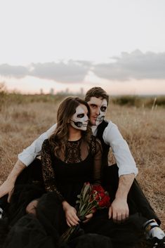 two people sitting on the ground with their faces painted like skulls and roses in front of them