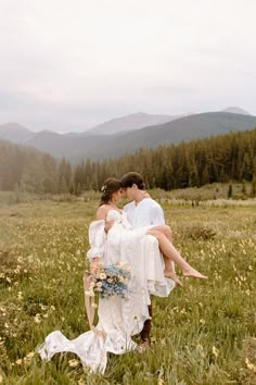 a bride and groom are sitting in a field with mountains in the backgroud