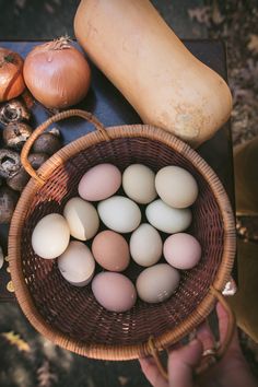 a person holding a basket filled with eggs next to some mushrooms and other food items