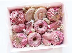 a pink box filled with lots of donuts covered in frosting and sprinkles