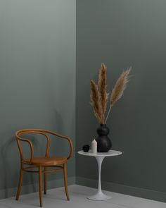 a chair next to a table with a vase on it and a plant in the corner