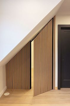 an empty room with wooden slats on the walls, and a black door in the corner