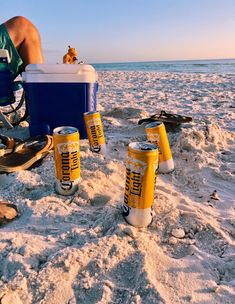 a man sitting on top of a beach next to beer cans