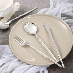 a white plate topped with silverware next to a cup and saucer on top of a table