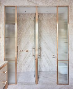 a bathroom with marble walls and flooring, two glass doors leading to the toilet