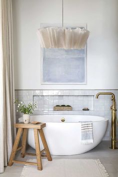 a white bath tub sitting next to a wooden stool in a bathroom under a painting