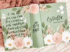 two green books with pink flowers on them sitting on a bed next to a blanket