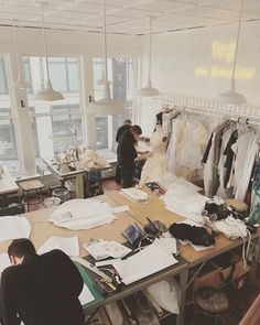 two people working in an office with clothes hanging on the wall and desks full of papers