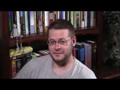 a man wearing glasses sitting in front of a bookshelf