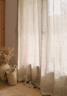 a white vase sitting on top of a rug next to a window with sheer curtains