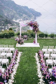 an outdoor ceremony setup with white chairs and purple flowers on the aisle, overlooking the ocean