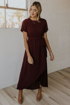 a woman standing in front of a window wearing a maroon dress with short sleeves and a high low neckline