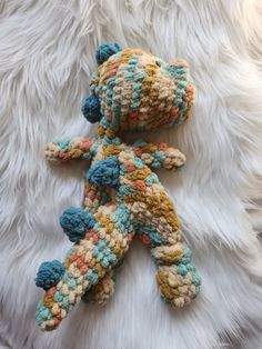 a crocheted teddy bear laying on top of a white fur covered floor next to a stuffed animal