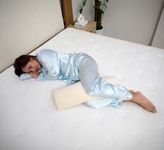 a woman laying on top of a mattress with a pillow over her head and arm