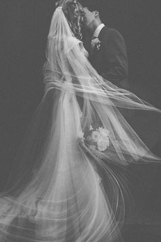 a bride and groom kissing in front of a black background with long flowing veils