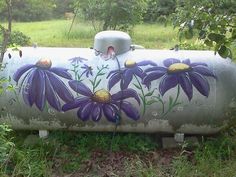 a large metal tank with purple flowers painted on it's side in the grass