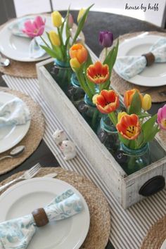 a table with plates, napkins and vases filled with colorful tulips