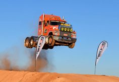 a big red truck is in the air over some dirt and flags on top of it