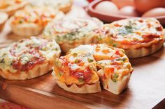 several mini quiches on a cutting board with eggs in the backgroung