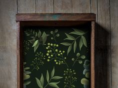 a wooden frame holding a painting with green leaves and berries on dark green wallpaper