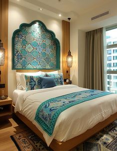 a large bed sitting next to a window in a bedroom under a blue and green headboard