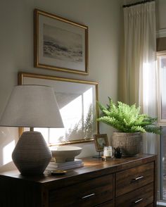 a table with a lamp, vase and pictures on it in front of a window