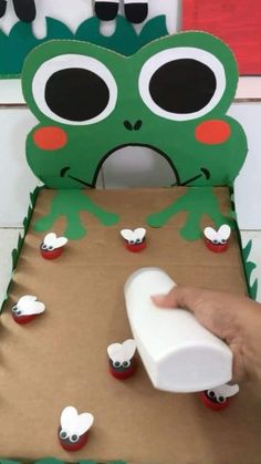 a paper cut out of a green frog with eyes and nose sitting on top of a cardboard box