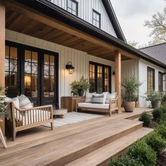 a wooden deck with two chairs and pillows on it next to a white house that has black doors