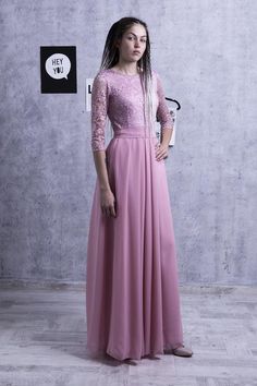 a woman standing in front of a wall wearing a long pink dress with sheer sleeves