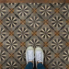 a person standing on top of a wooden floor next to a tiled floor with different colors and shapes