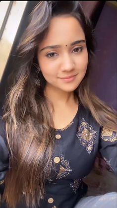 a young woman with long hair wearing a black dress and gold accents is posing for the camera