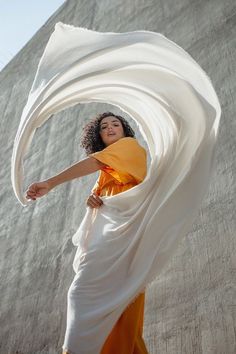 a woman in an orange and white dress with her arms spread out to the side