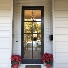 two red flower pots sitting on the side of a white house with a glass door