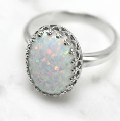 "This gorgeous white pinfire opal sits in a sterling silver 14 x 10mm (9/16\" x 3/8\") crown ring bezel that comes in 6, 7, 8, and 9 US ring sizes. The opal is lab-created with tones of sparkle in shades of pink, blue, lavender and green. Please read more about lab-created opals below. Opals are the birthstone of October but they are also known as the gem of choice by most and loved by many. If you have any questions please do not hesitate to contact me. What is a lab-created opal... Lab-created Classic White Cabochon Opal Ring, Classic White Opal Ring With Birthstone, Classic White Opal Birthstone Ring, Classic White Opal Jewelry, White Cabochon Opal Ring In Sterling Silver, White Opal Cabochon Ring In Sterling Silver, White Oval Cabochon Opal Ring, White Cabochon Opal Ring, White Opal Ring As A Gift