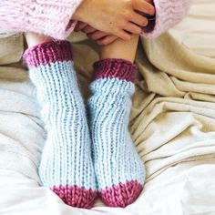 a woman wearing pink and blue socks with her hands on her knees while sitting on a bed