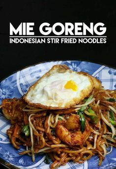 a blue and white plate topped with noodles and an egg on top of fried noodles