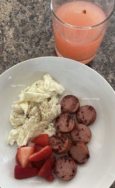 a white plate topped with sausage and strawberries next to a glass of orange juice