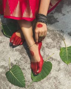 a woman's feet with red paint on them and green leaves around her ankles