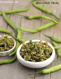 two small white bowls filled with food on top of a wooden table next to green beans