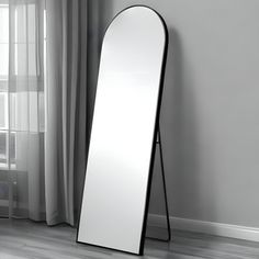 a large mirror leaning against the wall next to a window with curtains on either side