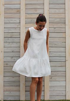 a woman standing in front of a wooden fence wearing a white dress with tiered ruffles