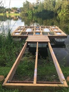 a wooden raft sitting on top of a lake next to grass and trees in the background