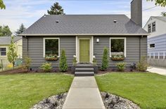 a small gray house with green doors and grass on the front lawn, next to a sidewalk