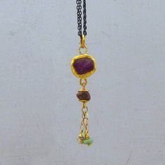 "A whimsical and colorful design gives this pendant an air of playfulness. A rough Ruby gemstone serves as the centerpiece, wrapped with 24k solid gold combined with purple Sapphire bead and rough green Emerald beads hanging on 14k gold chain that dangle freely for eye-catching movement. The back of the pendant made of 9k solid gold. The pendant hangs on silver oxidized chain with 14k gold hoop claps. ~ Pendant height: 2\" (52 mm). ~ Pendant width: 0.47\" (12 mm) ~ Chain length : 20.5\" ( 52 cm). The necklace will be packed in a gift box ready to be given as a gift, and will be shipped via EMS (express mail service) that usually takes 5-8 days to arrive. ▶ View my other necklaces here: https://www.etsy.com/il-en/shop/Omiya?section_id=7425982&ref=shopsection_leftnav_3 Please contact me with Sapphire Necklace Pendants, Emerald Bead, Purple Sapphire, Ruby Pendant, Gold Charm Necklace, Sapphire Pendant, Ruby Gemstone, Green Emerald, Silver Pendant Necklace