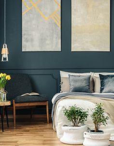 a bedroom with two paintings hanging on the wall above the bed and potted plants