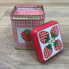 two tins with strawberries on them sitting next to each other in front of a wooden table