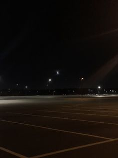 an empty parking lot at night with street lights in the distance and no cars on it